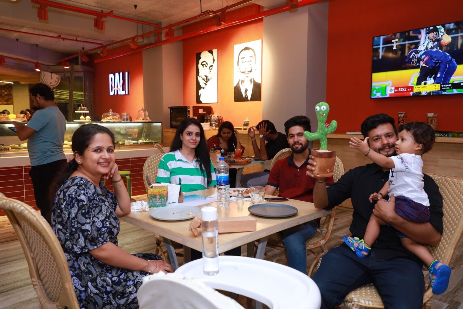 Guests sharing a table at Dali, with portrait artworks on the red wall behind.