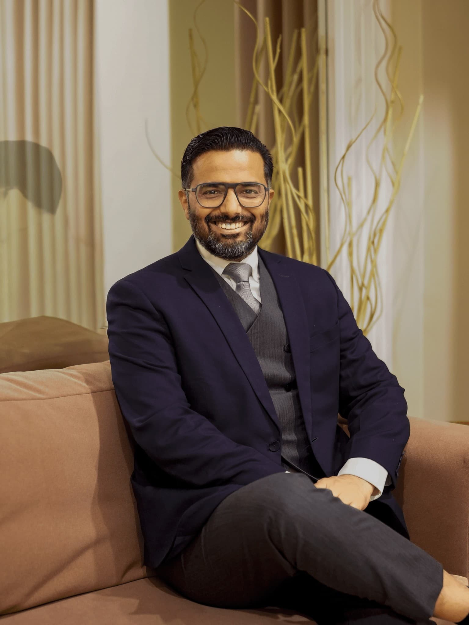 Amit Kandwal, in a dark suit and tie, seated on a sofa and smiling.
